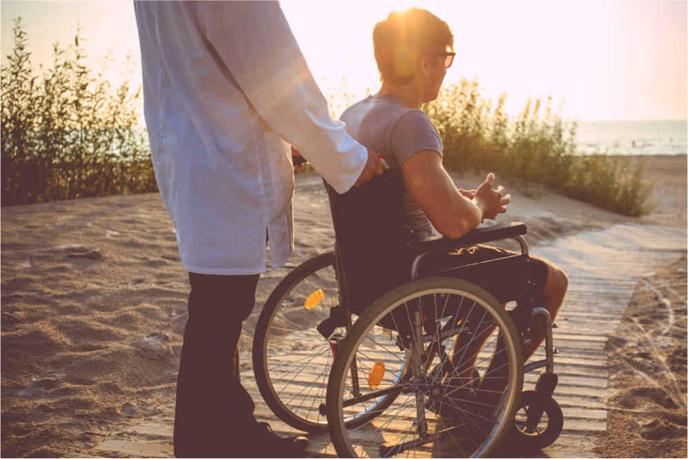 doctor pushing a patient in a wheelchair through a sand path